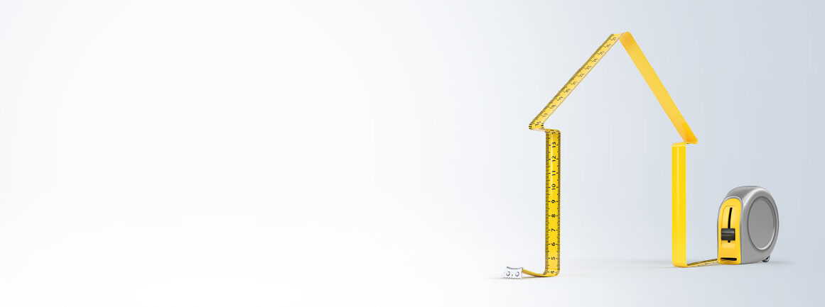 Ein Maßband hat die Form eines Hauses, wobei sich der Werkzeugkörper an der Basis befindet. Das gelbe Band bildet Dach und Wände vor einem hellgrauen Hintergrund und suggeriert so Heimwerkerkonzepte.