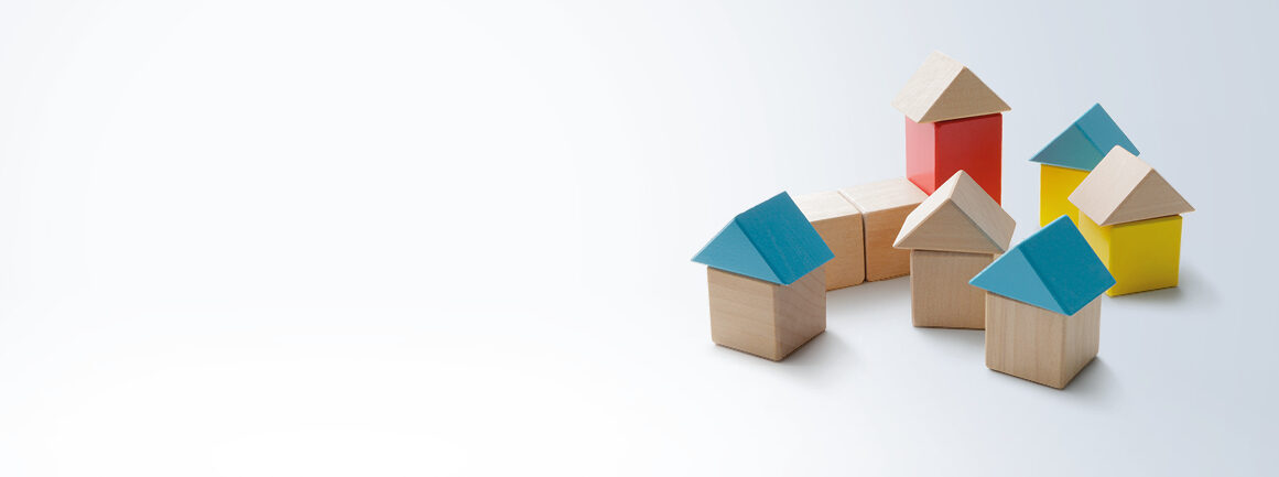 Spielzeug-Holzhäuser mit bunten Dreiecksdächern sind auf einem hellen Hintergrund angeordnet, wobei drei Häuser mit blauen Dächern, ein Haus mit roten Dächern und ein Haus mit gelben Dächern eine verspielte und minimalistische Szene schaffen.