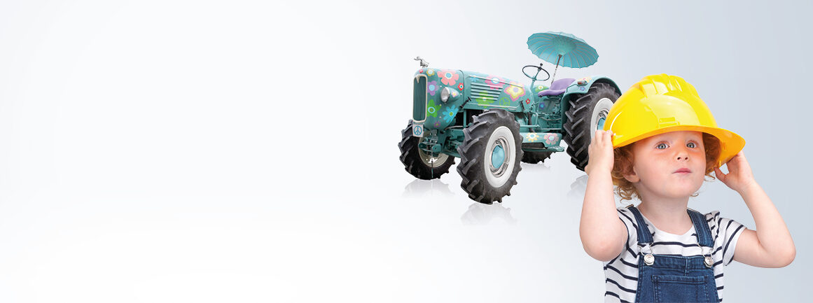 Ein Kind mit gelbem Bauhelm blickt nach oben. Im Hintergrund ist ein dekorativer Traktor zu sehen, der mit Blumen bemalt und mit einem kleinen blauen Regenschirm ausgestattet ist. Der Hintergrund ist hellgrau.