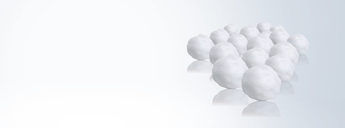 Mehrere weiße Schneebälle sind versetzt auf einer reflektierenden Oberfläche am rechten Bildrand angeordnet. Der Hintergrund weist einen hellen Farbverlauf von Weiß zu Zartblau auf.