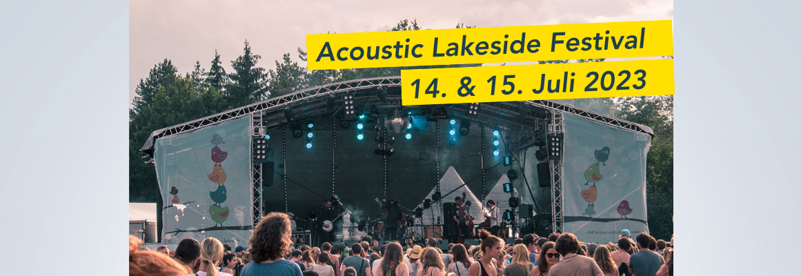 Open-Air-Konzert mit einer großen Menschenmenge vor der Bühne. Auf dem Schild steht „Acoustic Lakeside Festival 14. & 15. Juli 2023“. Im Hintergrund sind hohe Bäume unter einem bewölkten Himmel zu sehen.