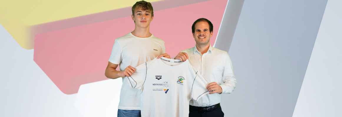 Zwei lächelnde Männer stehen da und halten ein weißes Sporttrikot zwischen sich. Einer trägt ein weißes T-Shirt, der andere ein weißes Hemd. Im Hintergrund sind große abstrakte geometrische Formen in Pastellfarben zu sehen.