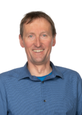 Lächelnder Mann mit kurzen braunen Haaren und blauem Hemd mit Kragen.