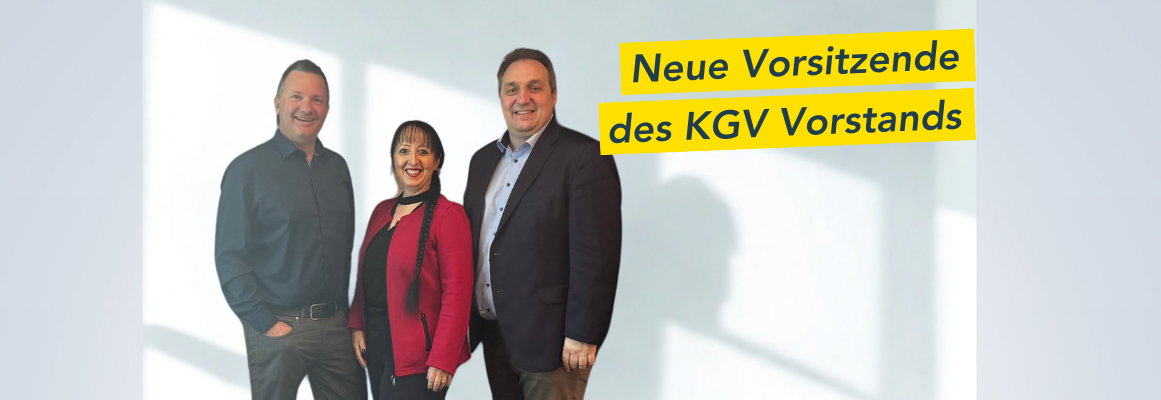 Drei Personen stehen lächelnd da, zwei Männer und eine Frau. Sie tragen halbformelle Kleidung. In der oberen rechten Ecke befindet sich ein gelbes Banner mit der Aufschrift „Neue Vorsitzende des KGV-Vorstands“.